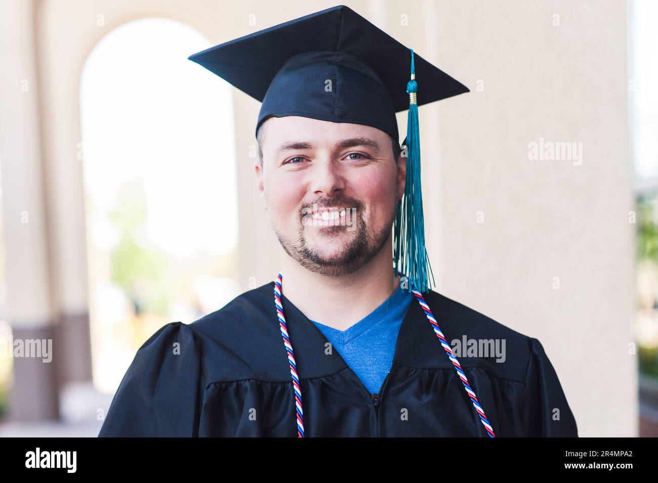 Portrait souriant d'un homme diplômé en casquette et robe noires Banque D'Images