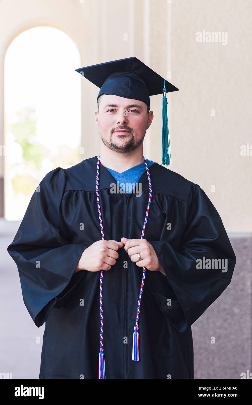 Portrait souriant d'un homme diplômé en casquette et robe noires Banque D'Images