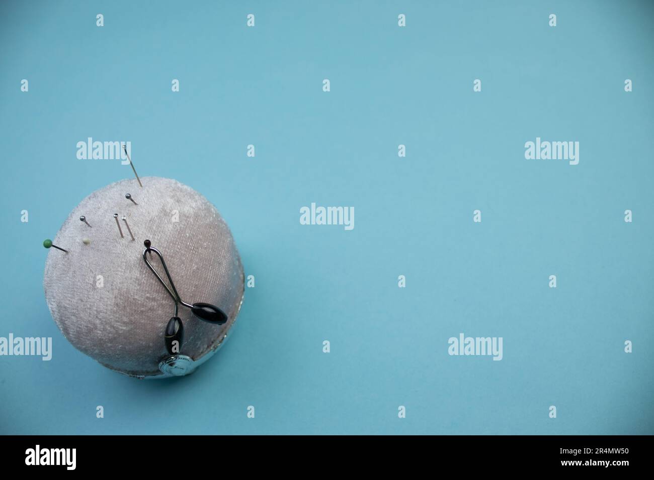 Coussin de broche rose avec broches dessus, photographié par le dessus, placé sur le bord de l'arrière-plan bleu. Banque D'Images