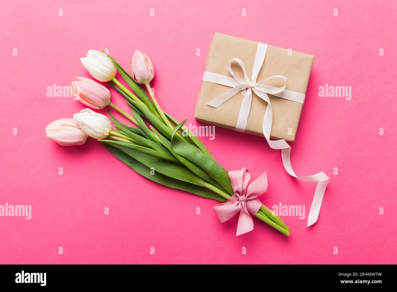 Fleurs de tulipes roses et boîte cadeau ou cadeau sur fond de table coloré. Fête des mères, anniversaire, Fête des femmes, concept de célébration. Espace pour texte haut vi Banque D'Images