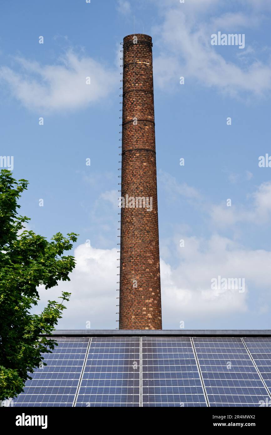 un toit recouvert de panneaux solaires devant une vieille cheminée en briques industrielles contre un ciel bleu avec des nuages à cologne ehrenfeld Banque D'Images