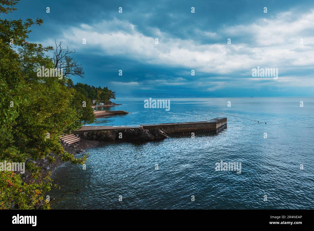 Jetée en pierre de béton à la ville de Lovran dans le golfe de Kvarner de la mer Adriatique au coucher du soleil avec ciel couvert de tempête Banque D'Images