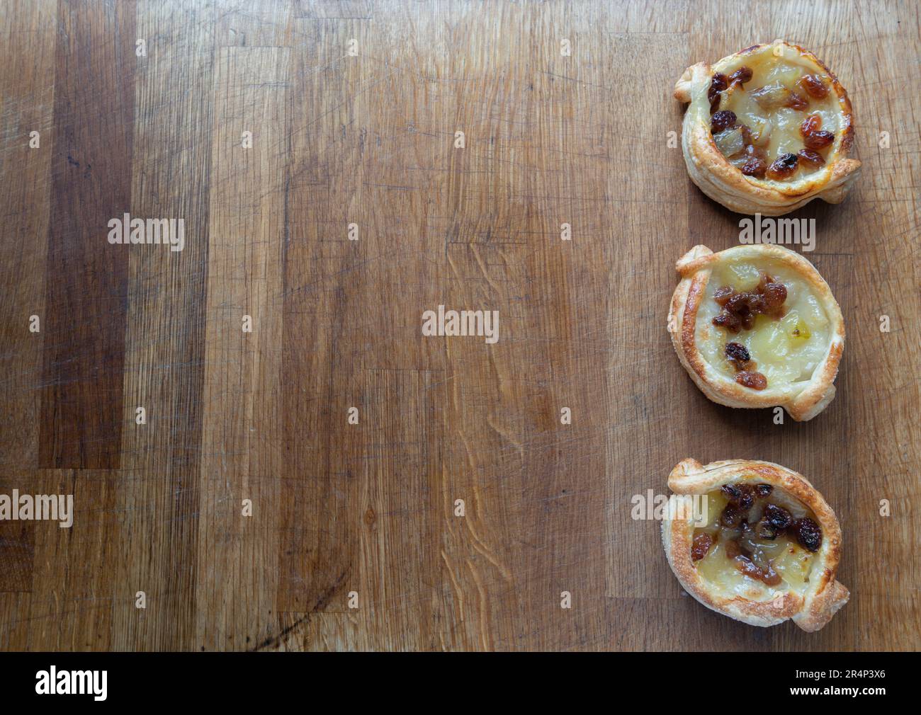 Laissez-vous tenter par les saveurs irrésistibles de ces pâtisseries feuilletées danoises, généreusement garnies de pommes et de sultanines, présentées sur un charmant hacher en bois Banque D'Images