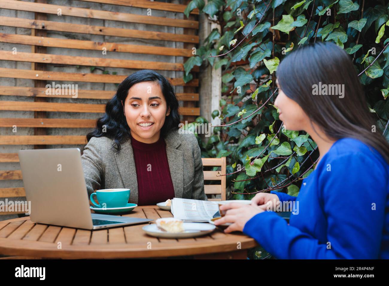 Conversation sur la sécurité financière: Jeune femme Latina vendant l'assurance vie à une autre femme dans un café confortable Banque D'Images