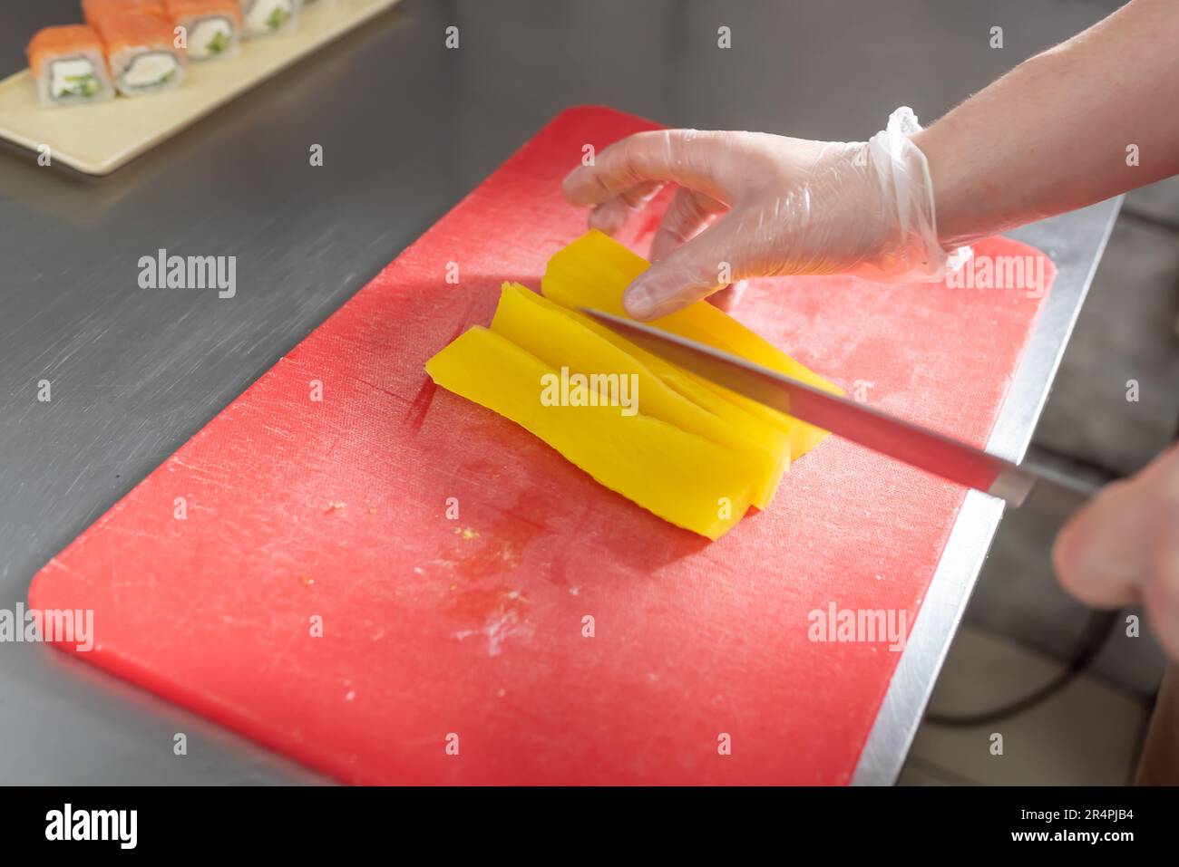 Le cuisinier coupe des daikon marinés pour des sushis sur un tableau rouge. Photo de haute qualité Banque D'Images