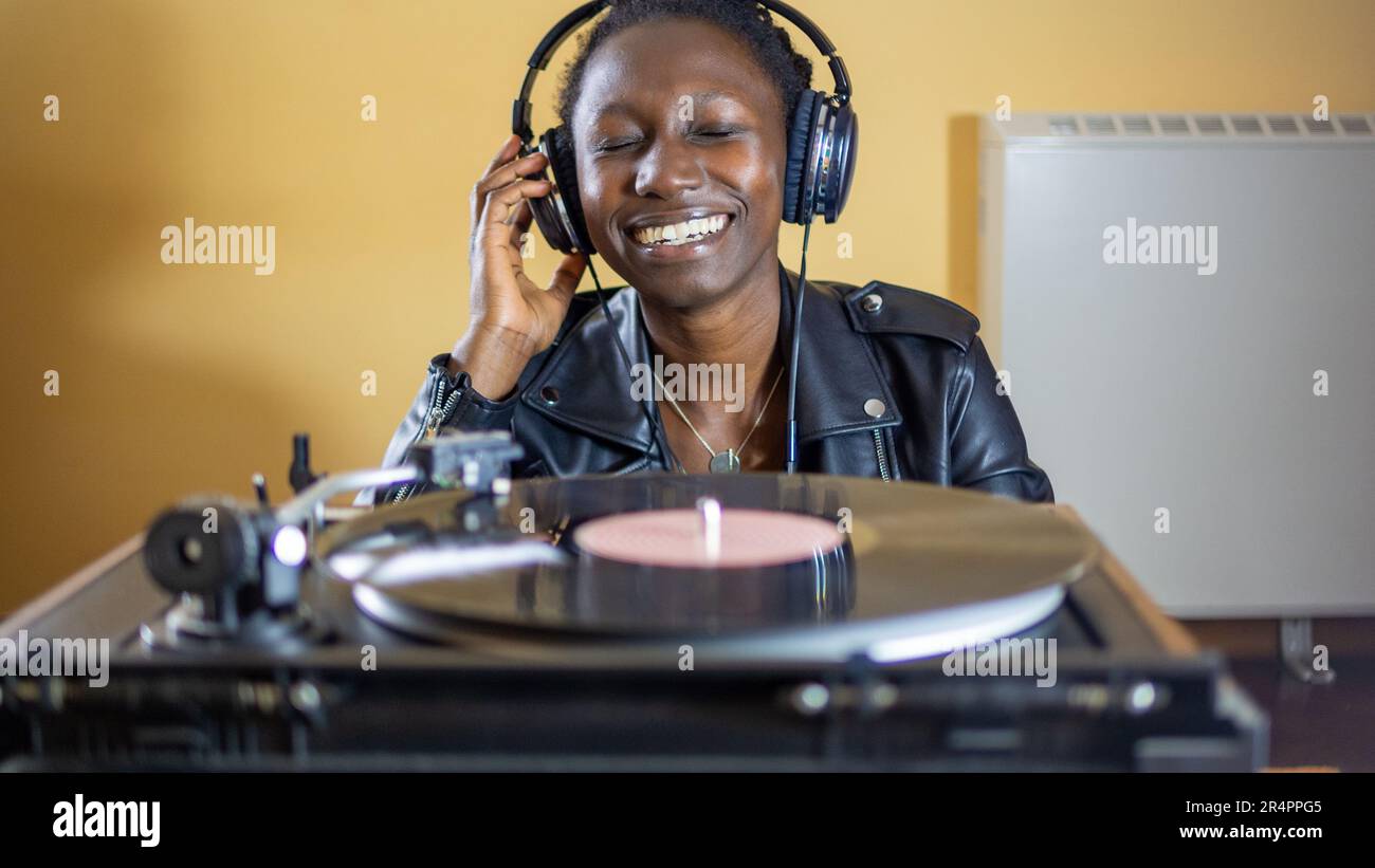jeune femme portant une veste en cuir utilisant un casque tout en jouant un disque en vinyle sur une plaque tournante d'époque Banque D'Images