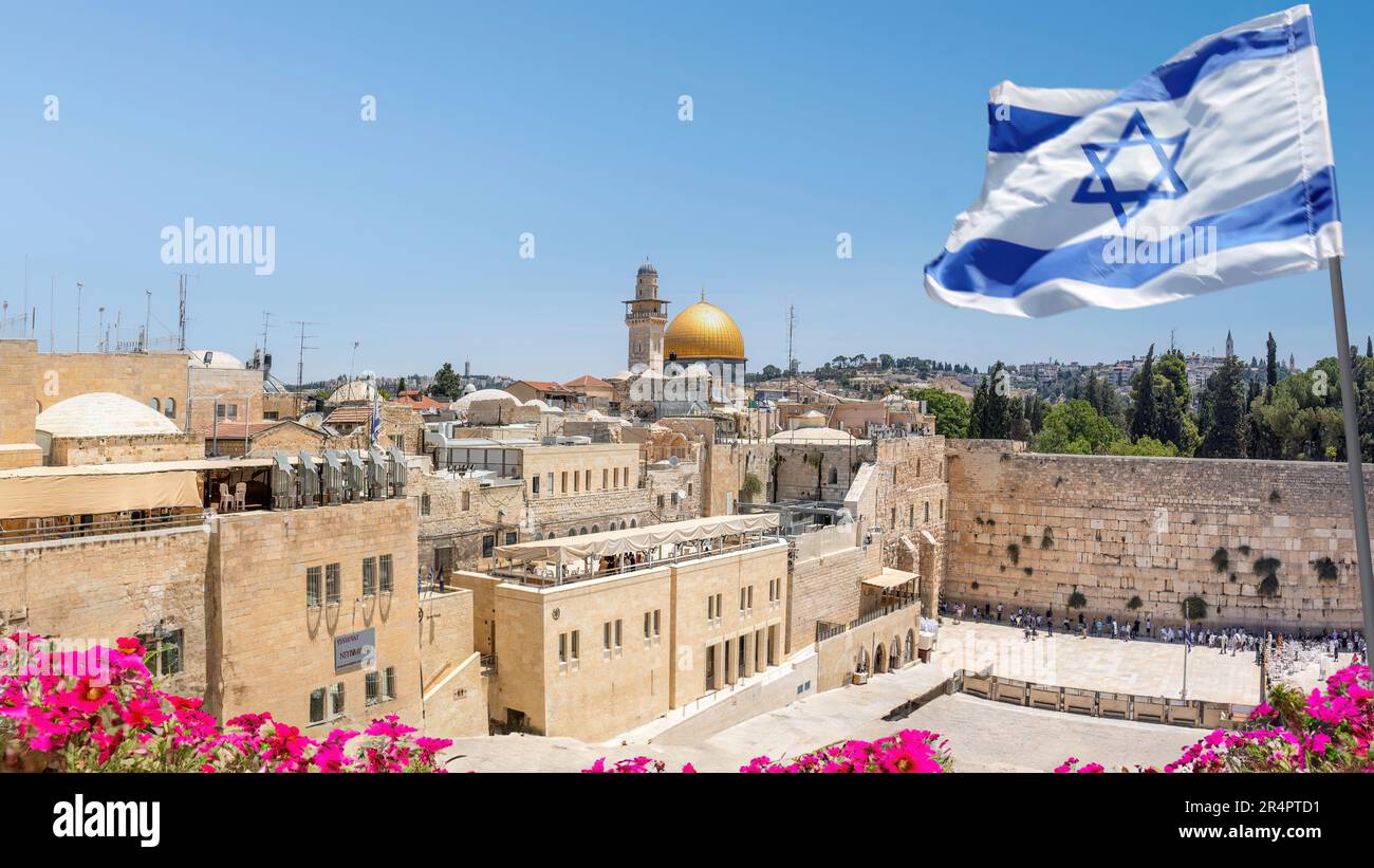 Jérusalem, Israël; 28 mai 2023 - un drapeau israélien souffle dans le vent tandis que les croyants orthodoxes juifs lisent la Torah et prient face au mur occidental. Banque D'Images