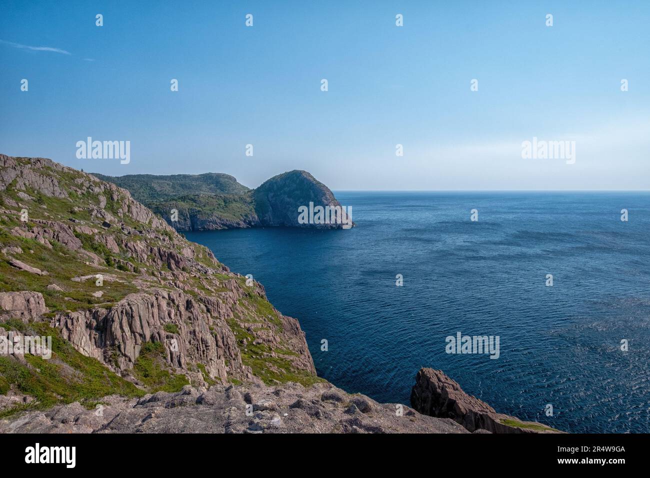 L'océan Atlantique bleu profond avec des vagues qui s'écrasant sur une île rocheuse. La côte de la mer a de hautes falaises accidentées avec des collines couvertes de collines. Banque D'Images