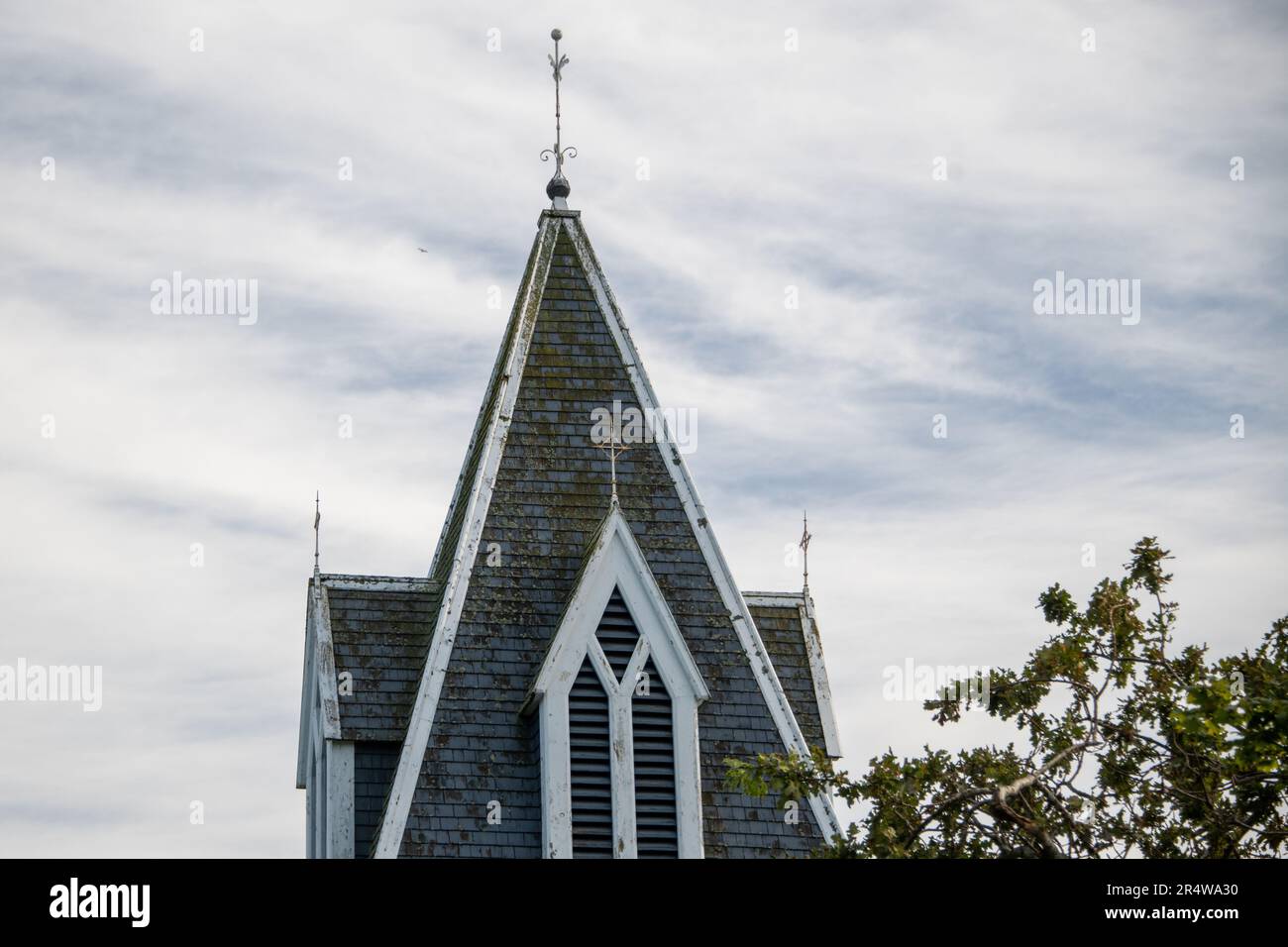 Une place catholique en bois de couleur bleu foncé est le clocher d'un bâtiment religieux. Les fenêtres extérieures décoratives sont dotées de garnitures blanches. Il y a un grand arbre à côté Banque D'Images
