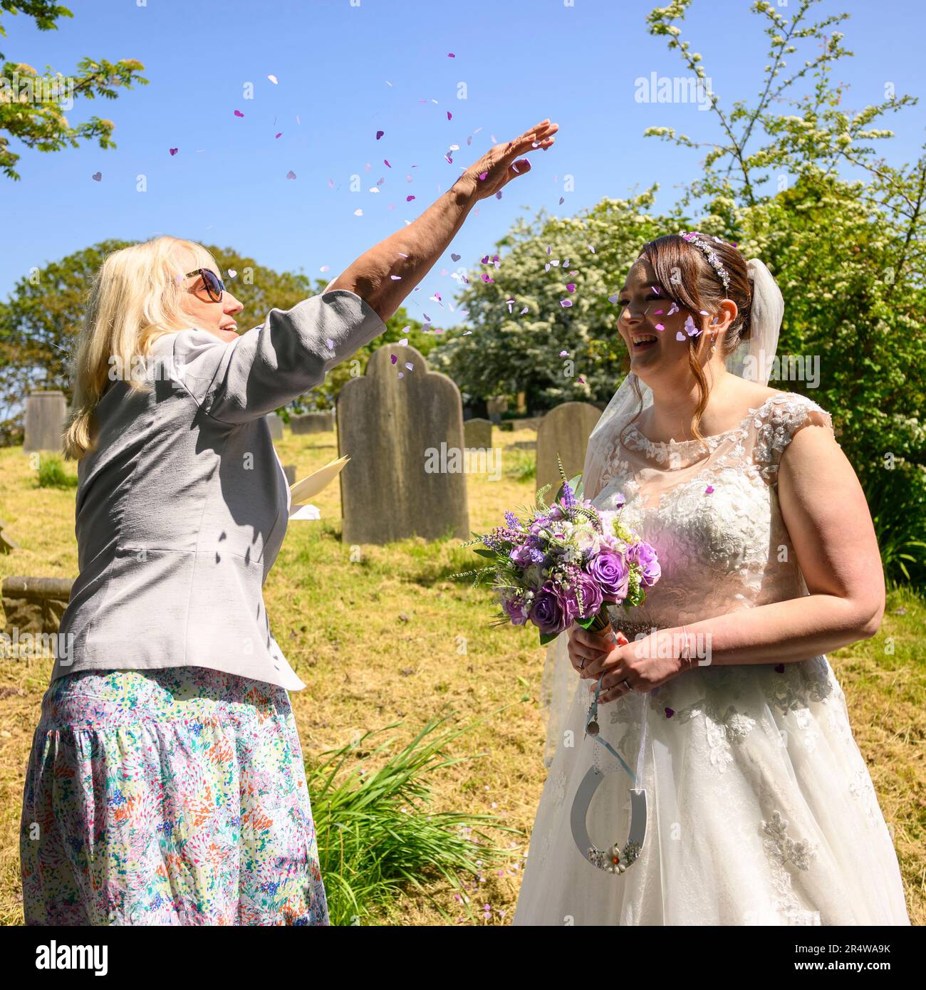 Une femme jette des confetti sur une mariée dans une robe de mariage le jour du mariage Banque D'Images