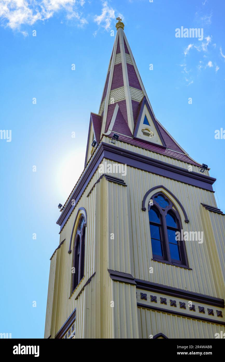 Un grand carré catholique en bois de couleur jaune en forme de clocher d'un bâtiment religieux. Les fenêtres décoratives extérieures sont décorées de rouge. Banque D'Images