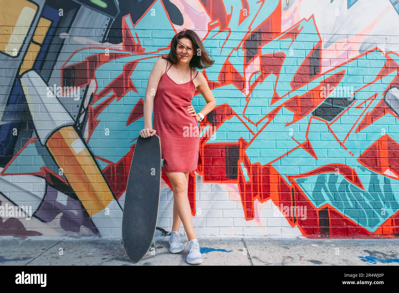 Jeune femme en robe rouge court posant sur fond de murs avec graffiti. Banque D'Images