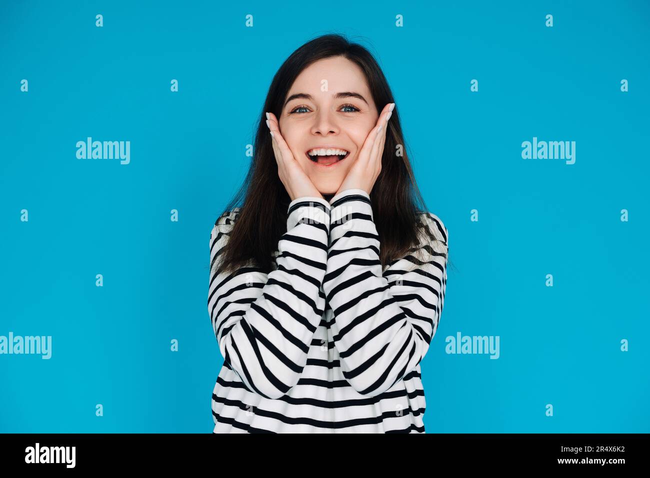 Portrait expressif d'une jeune femme surprise et joyeuse avec palmiers sur pommettes, isolé sur fond bleu. Banque D'Images