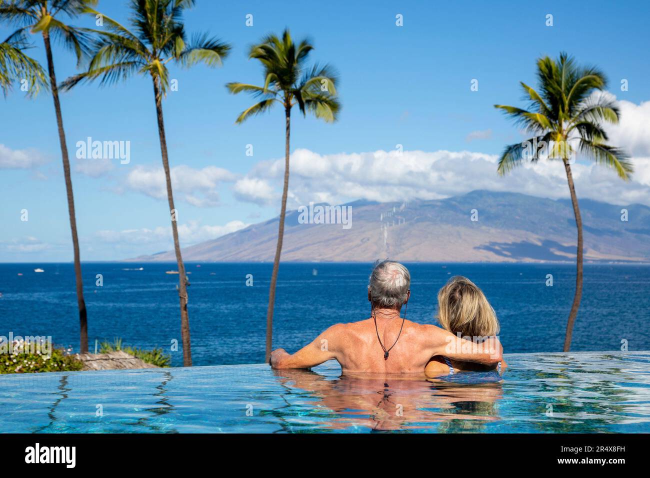 Vue prise de derrière un couple profitant de la vue sur l'océan depuis la piscine à débordement du four Seasons Resort Banque D'Images