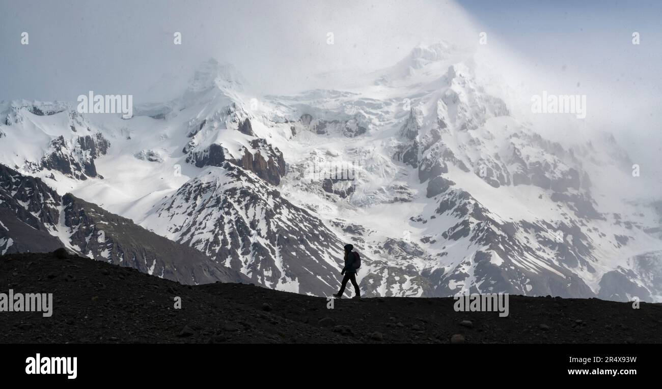 Silhouette d'une personne marchant le long d'une moraine glaciaire devant une grande montagne enneigée sur la côte sud de l'Islande ; Islande du Sud, Islande Banque D'Images