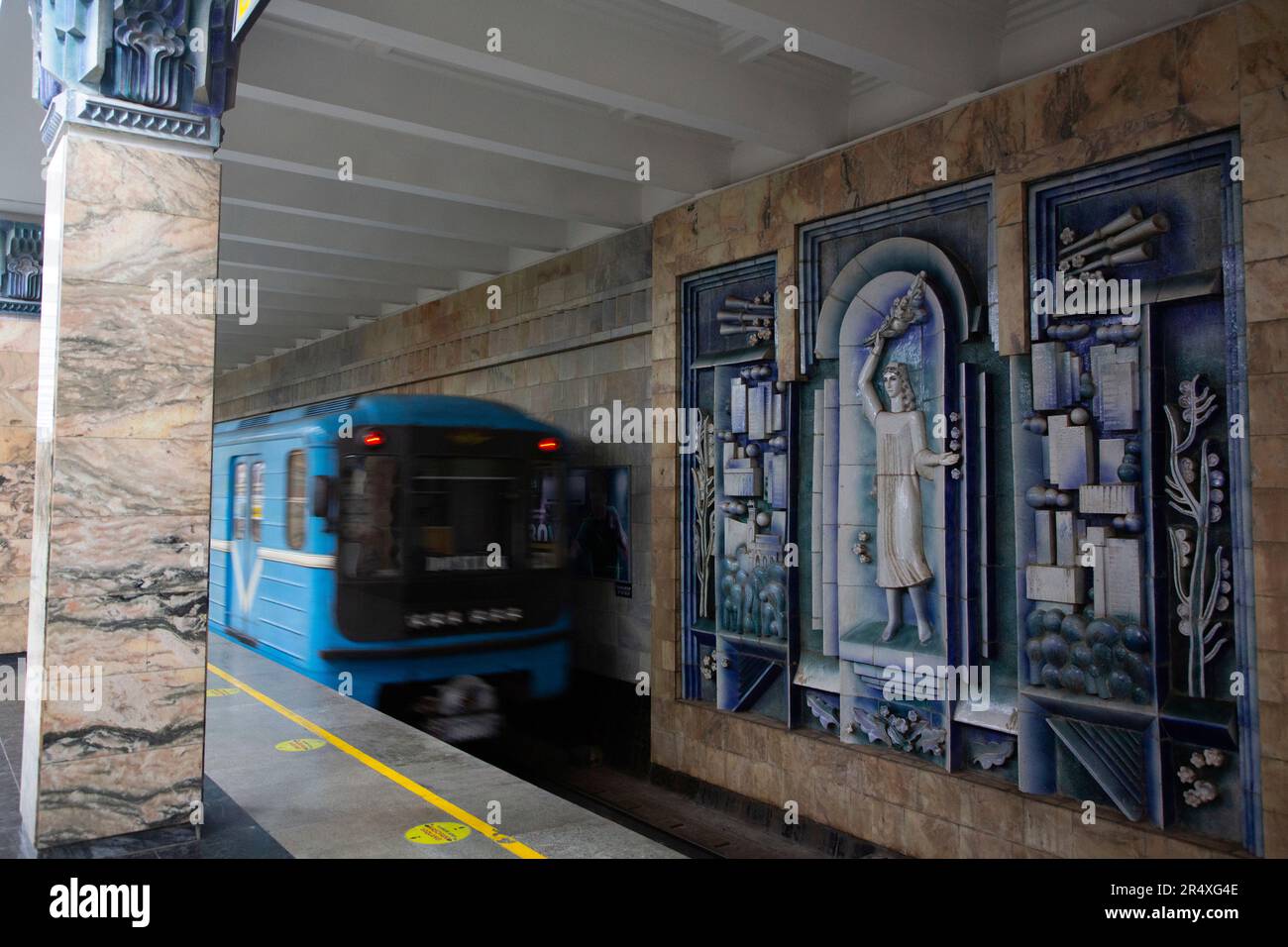 Train se déplace sur les voies devant des œuvres d'art sur les murs décorés de la gare de Toshkent pour le métro de Tachkent en Ouzbékistan ; Tachkent, Ouzbékistan Banque D'Images