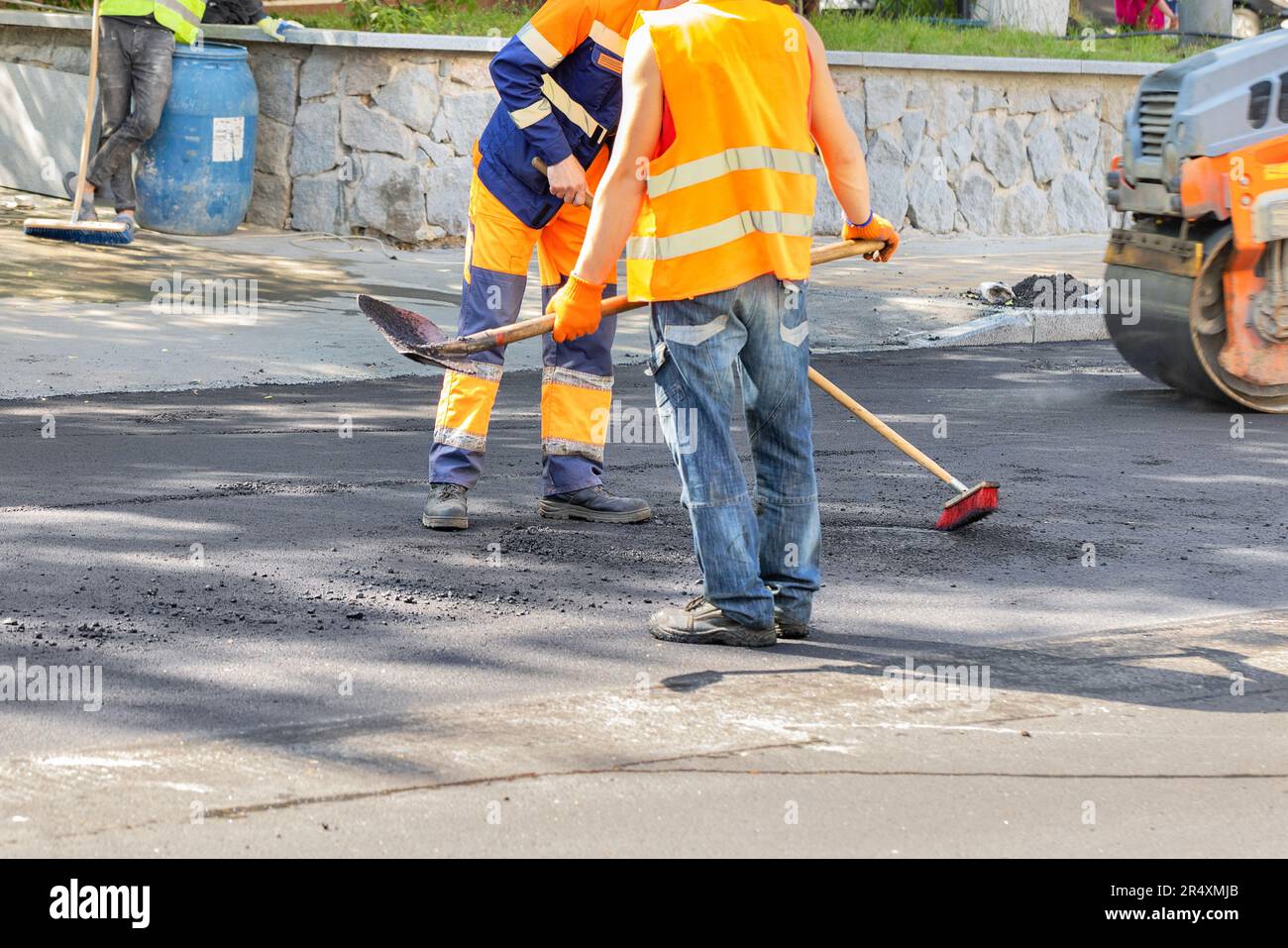 Les travailleurs réparent la route et nettoient la chaussée asphaltée asphaltez la route autour du trou d'égout à l'aide d'une brosse et d'une pelle par temps chaud. Banque D'Images