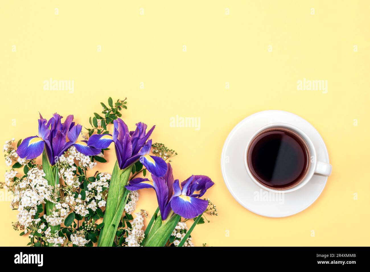 Tasse de café et bouquet de fleurs d'iris bleu sur fond jaune. Vue de dessus, plan d'agencement, espace de copie. Banque D'Images