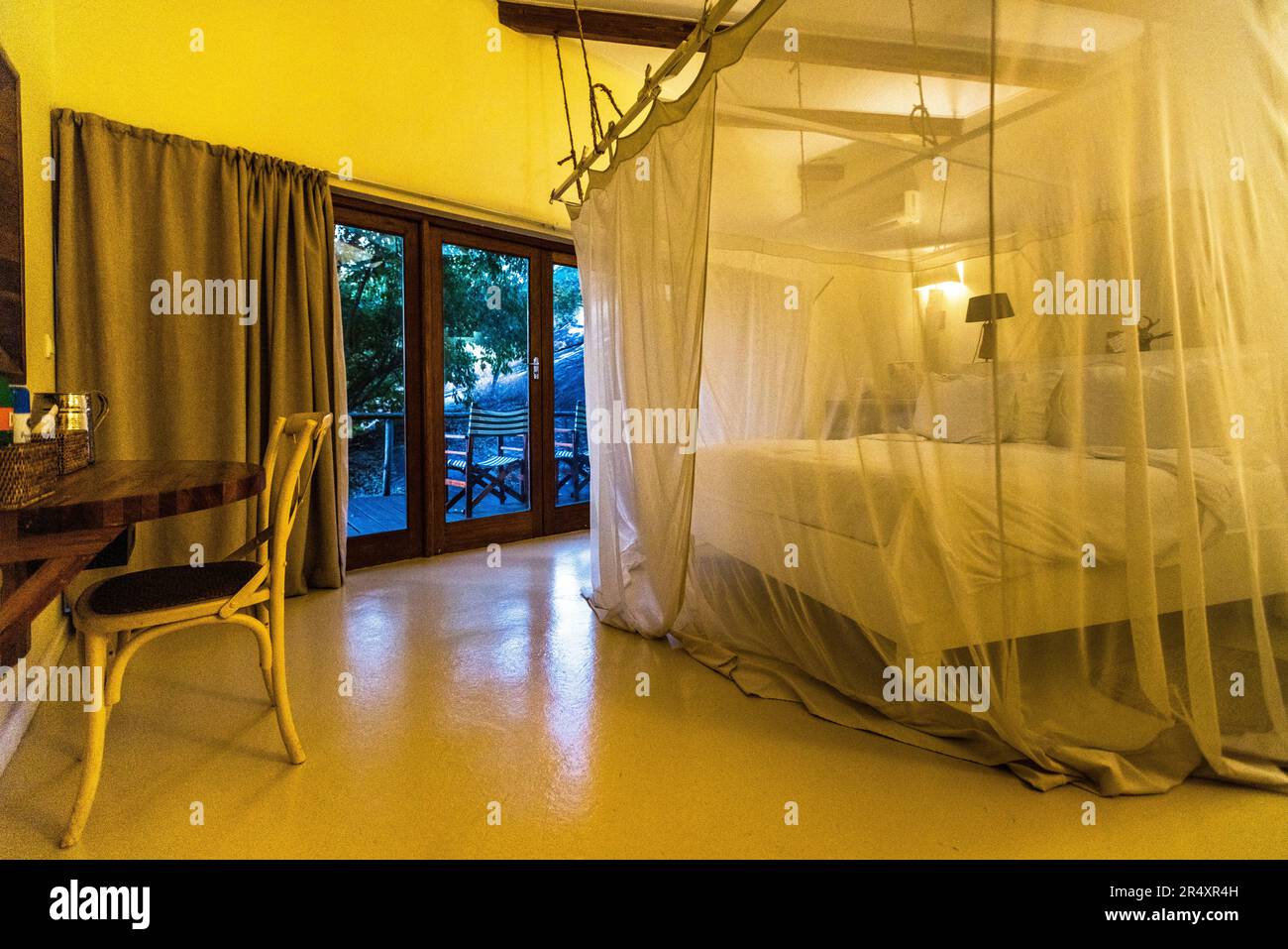 Une chambre avec une moustiquaire transparente au-dessus du lit se trouve dans une villa de la Pumulani Lodge (Robin Pope Safaris) sur le lac Malawi près de Cape Maclear, parc national du lac Malawi, Malawi ; une porte-fenêtre donne sur l'extérieur. Banque D'Images