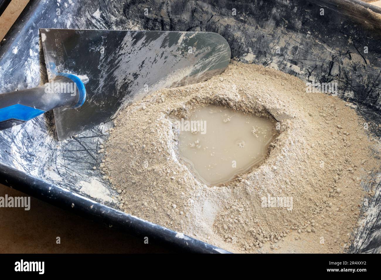 Poudre de ciment avec eau prête à être mélangée avec une truelle dans un bol en plastique, processus de fabrication de mortier. Banque D'Images