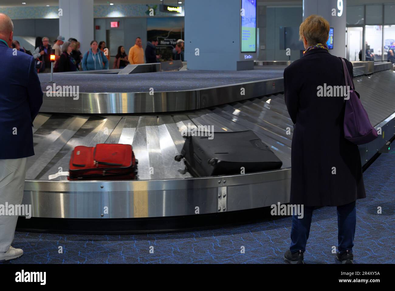 Les personnes qui attendent de récupérer leurs bagages dans un carrousel à bagages à la zone de retrait des bagages du terminal B de l'aéroport LaGuardia, New York. Banque D'Images