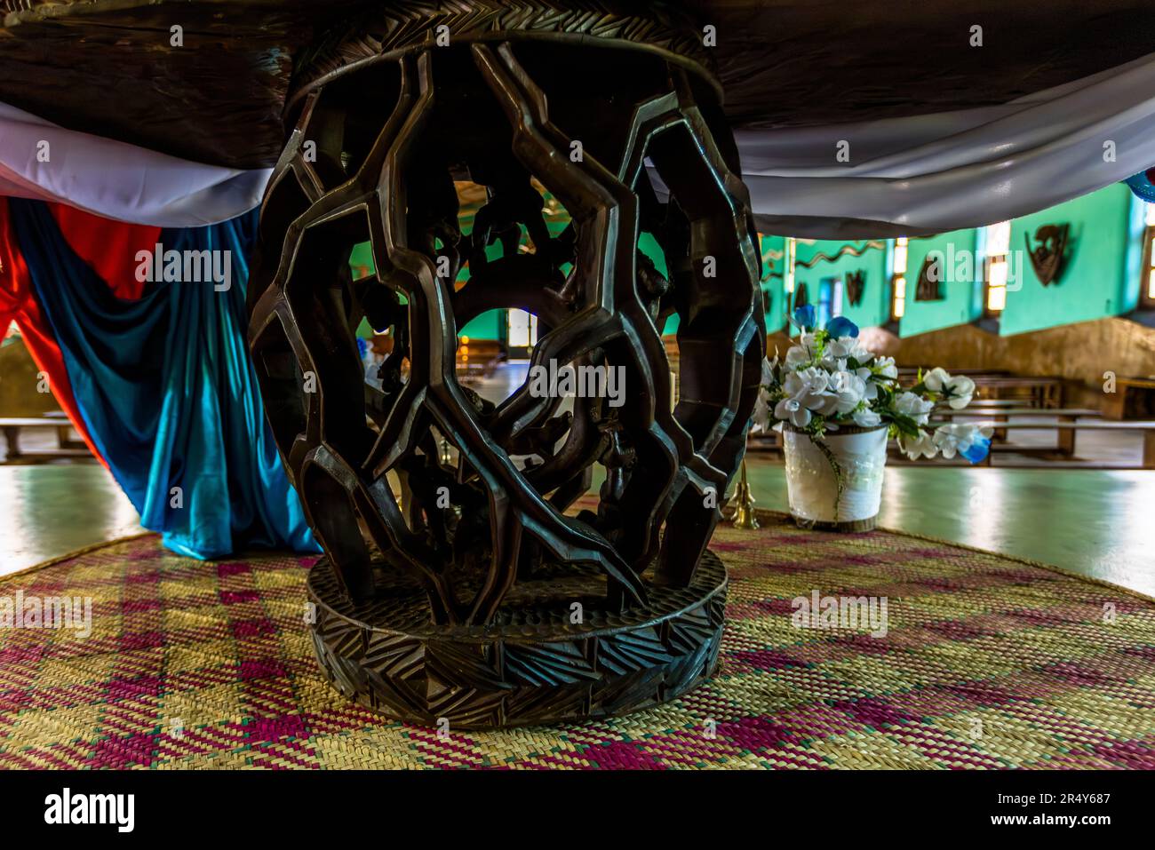 Un piédestal en bois finement sculpté et ajouré supporte une table dans l'église de la mission de Mua à Dedza, Malawi ; des masques sont accrochés au mur turquoise en arrière-plan. Banque D'Images