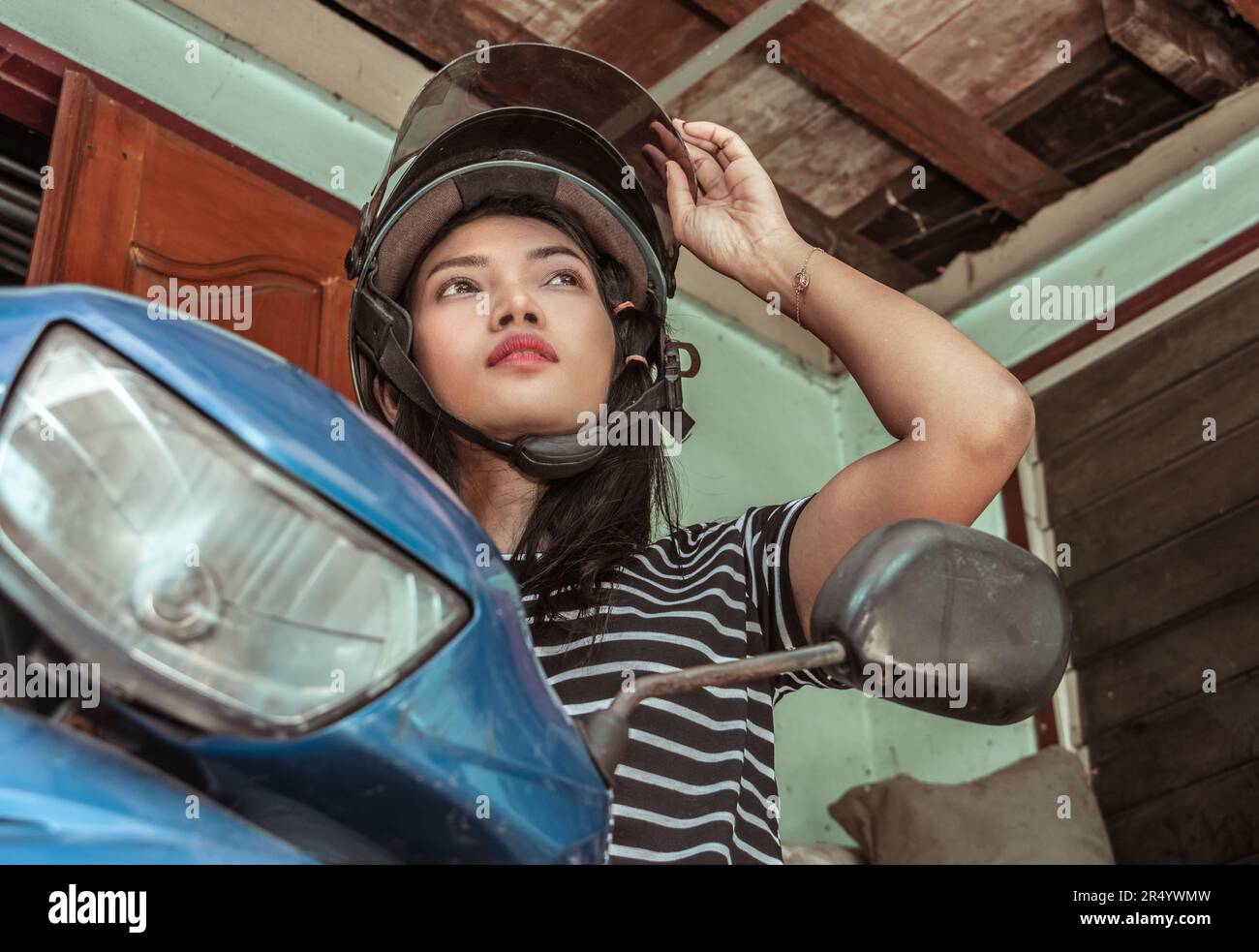 Une jeune femme avec un casque est assise sur une moto devant l'entrée de la maison Banque D'Images