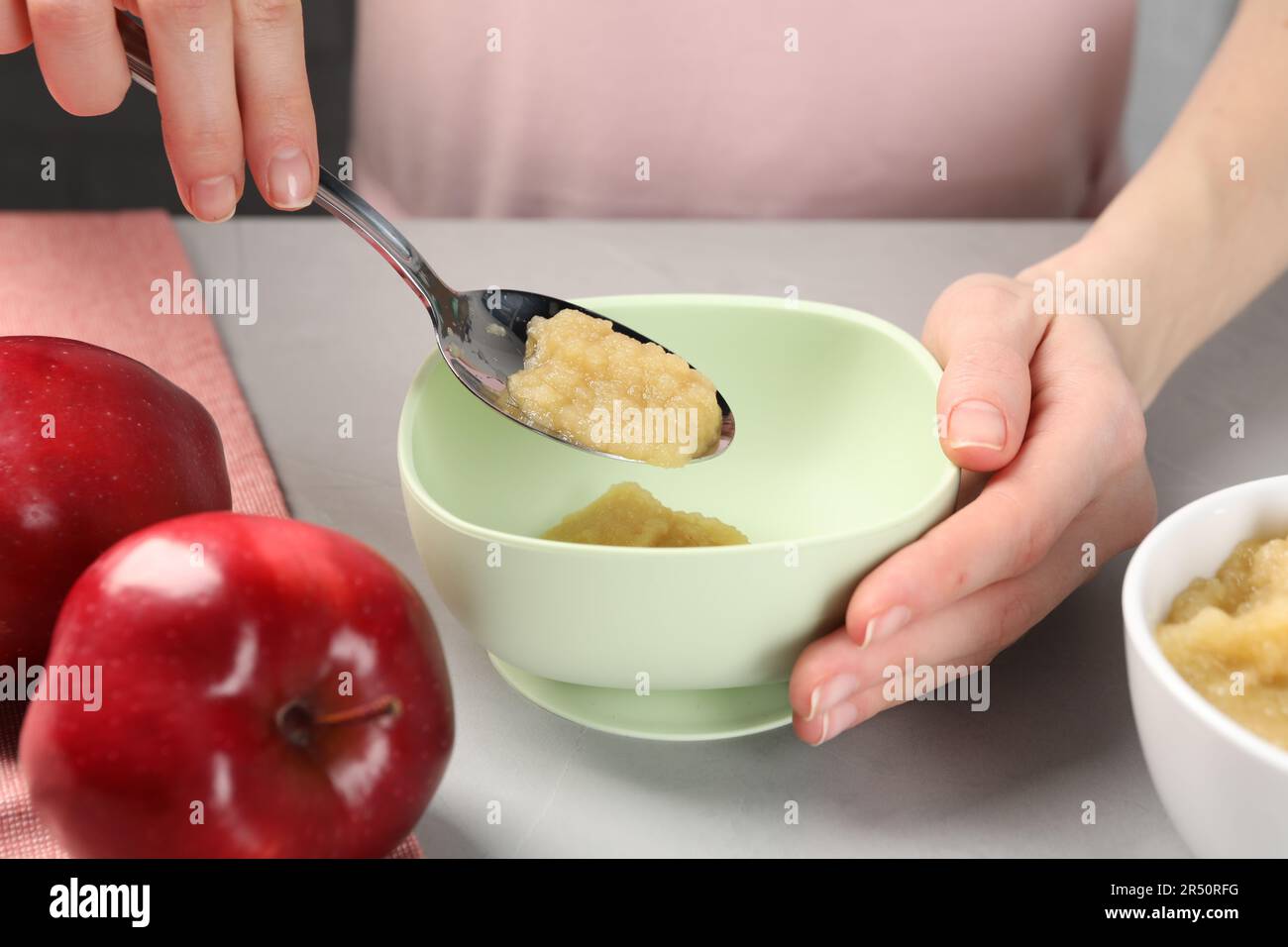 Une alimentation saine pour bébé. Femme mettant une délicieuse purée de pommes dans un bol à table gris clair, gros plan Banque D'Images