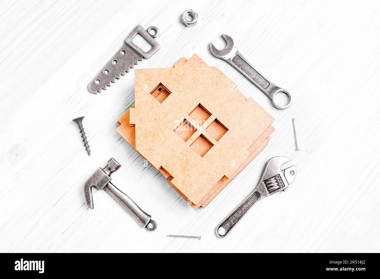 Vue de dessus d'un modèle de maison miniature en bois démontée et de petites répliques en acier de divers outils à main tels qu'un marteau, une scie, des clés, des écrous et des clous Banque D'Images