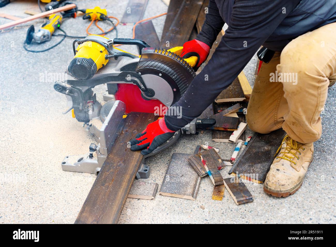 Un travailleur qualifié utilise une scie à onglet composée coulissante pour couper les revêtements de sol en bois sombre stratifiés à l'extérieur. Travail du bois, projets de bricolage, ou rénovation de la maison ba Banque D'Images