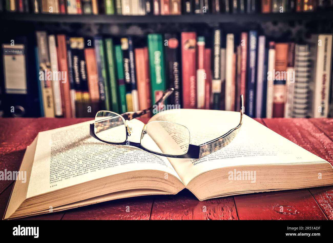 Ouvrez un livre et des lunettes avec des livres sur une étagère à l'arrière-plan. Faible profondeur de champ. Banque D'Images