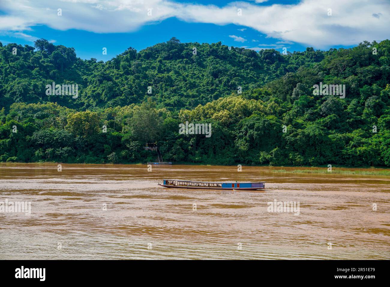 Un bateau lent traditionnel du Laos glisse à travers le bassin inférieur boueux du Mékong, entouré par la jungle tropicale luxuriante et la sérénité post-pluviale. Banque D'Images