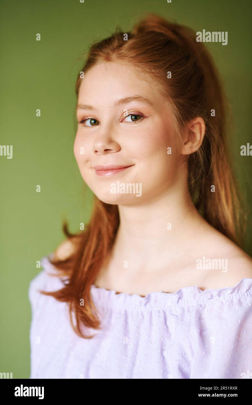 Portrait de beauté de la jolie jeune fille de 15 - 16 ans à poil rouge portant une robe pourpre posant sur fond vert Banque D'Images