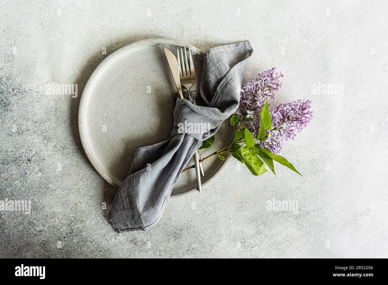Vue de dessus d'une table élégante avec fleurs de lilas fraîches, fourchette, couteau et serviette sur plaque grise sur fond gris Banque D'Images