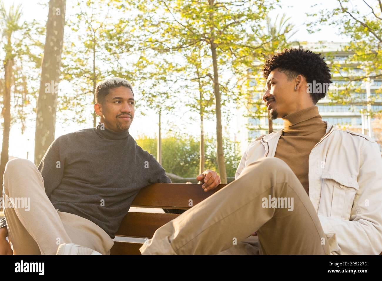 De jeunes amis Afro-américains assis sur un banc en bois et se regardant les uns les autres tout en discutant pendant une réunion dans un parc Banque D'Images