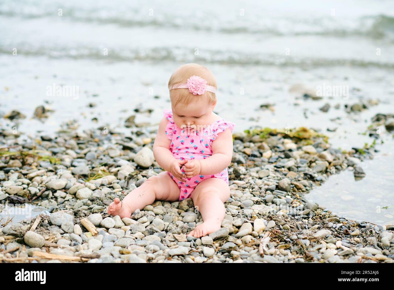 Portrait extérieur d'adorable petite fille jouant avec l'algue au bord de la rivière, portant un maillot de bain rose Banque D'Images