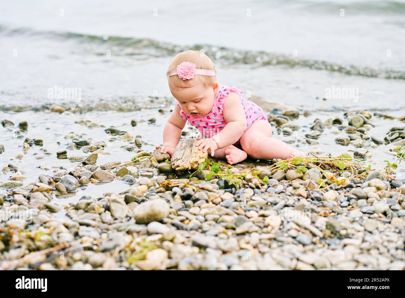 Portrait extérieur d'adorable petite fille jouant avec l'algue au bord de la rivière, portant un maillot de bain rose Banque D'Images