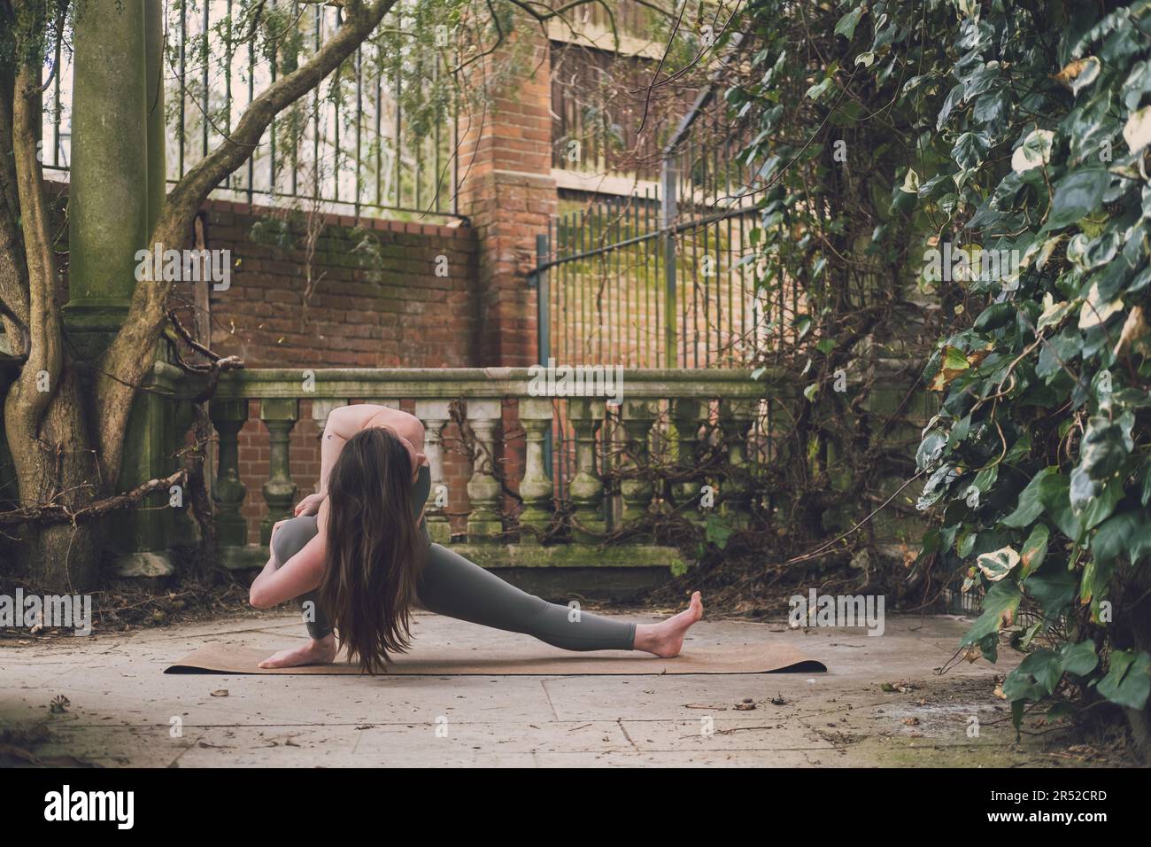 Une enseignante de yoga irlandaise pratiquant dans une fente latérale liée skandasana pose dans une terrasse d'un jardin historique à Hampstead Heath, Londres, dehors Banque D'Images