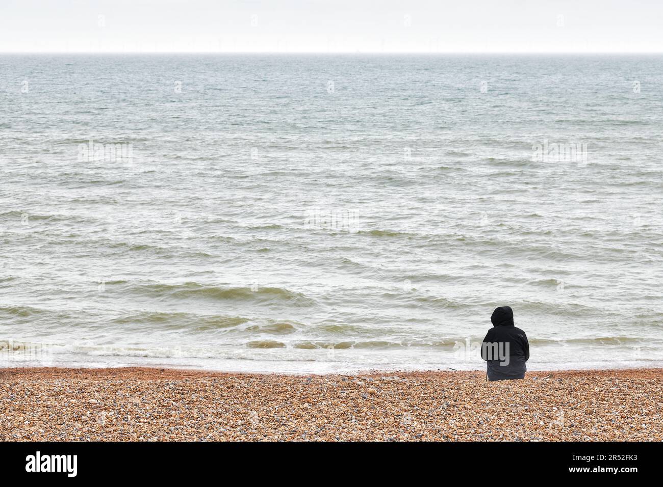 Une personne s'assoit seule sur la plage de galets lors d'une journée froide et grise à Brighton et Hove, sur la côte sud de l'Angleterre. Banque D'Images