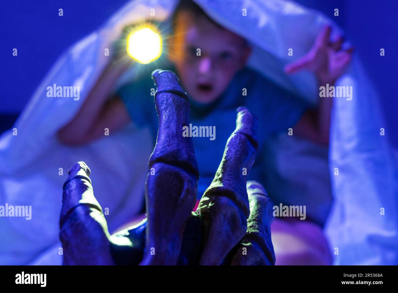 Un garçon effrayé avec une lampe de poche se cache sous une couverture de la main d'un monstre effrayant Banque D'Images