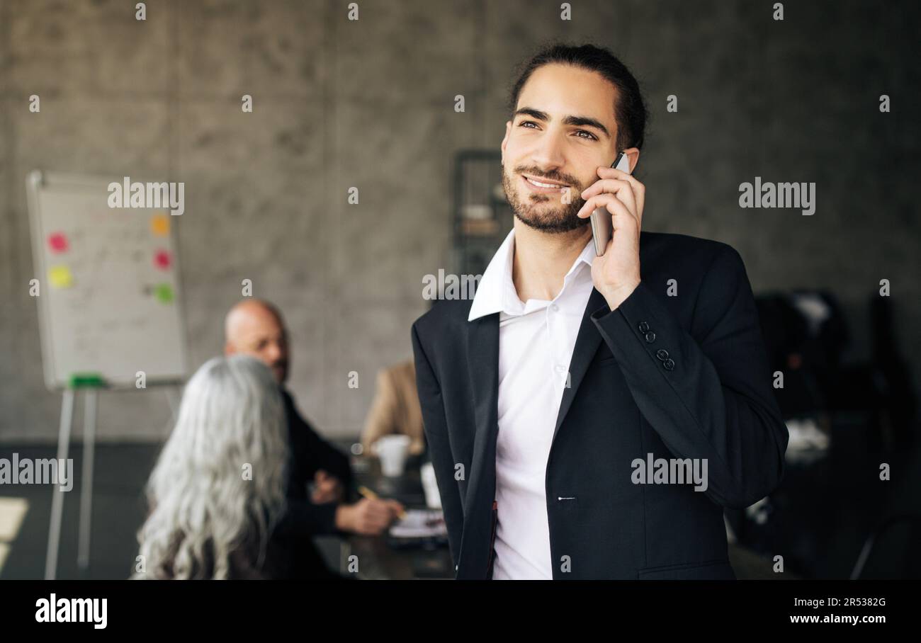 Jeune homme d'affaires arabe prospère parlant sur téléphone portable au bureau Banque D'Images