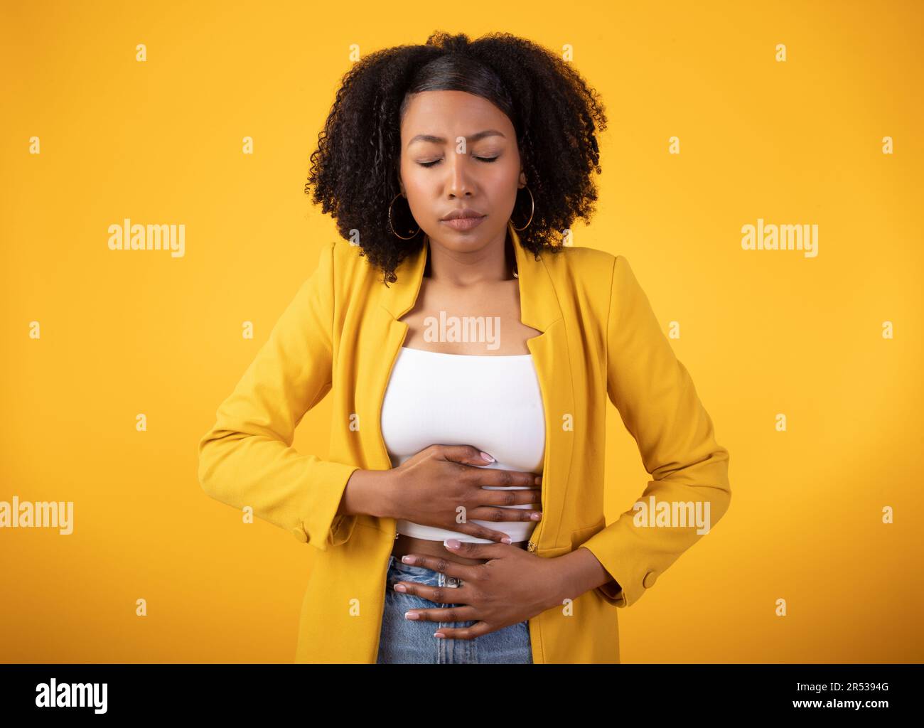Concept de stomachache. La dame noire touchant le ventre avec les yeux fermés, souffrant de douleur sur fond jaune Banque D'Images