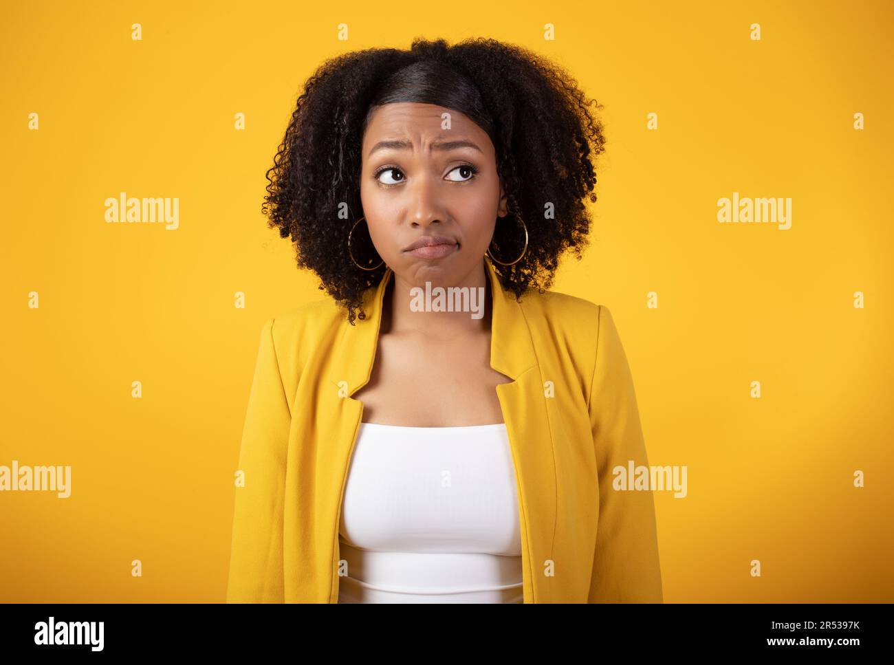 Jeune femme noire triste et attentionnés, regardant de côté sur fond jaune, imaginant quelque chose, se sentant douteuse ou contrariée Banque D'Images