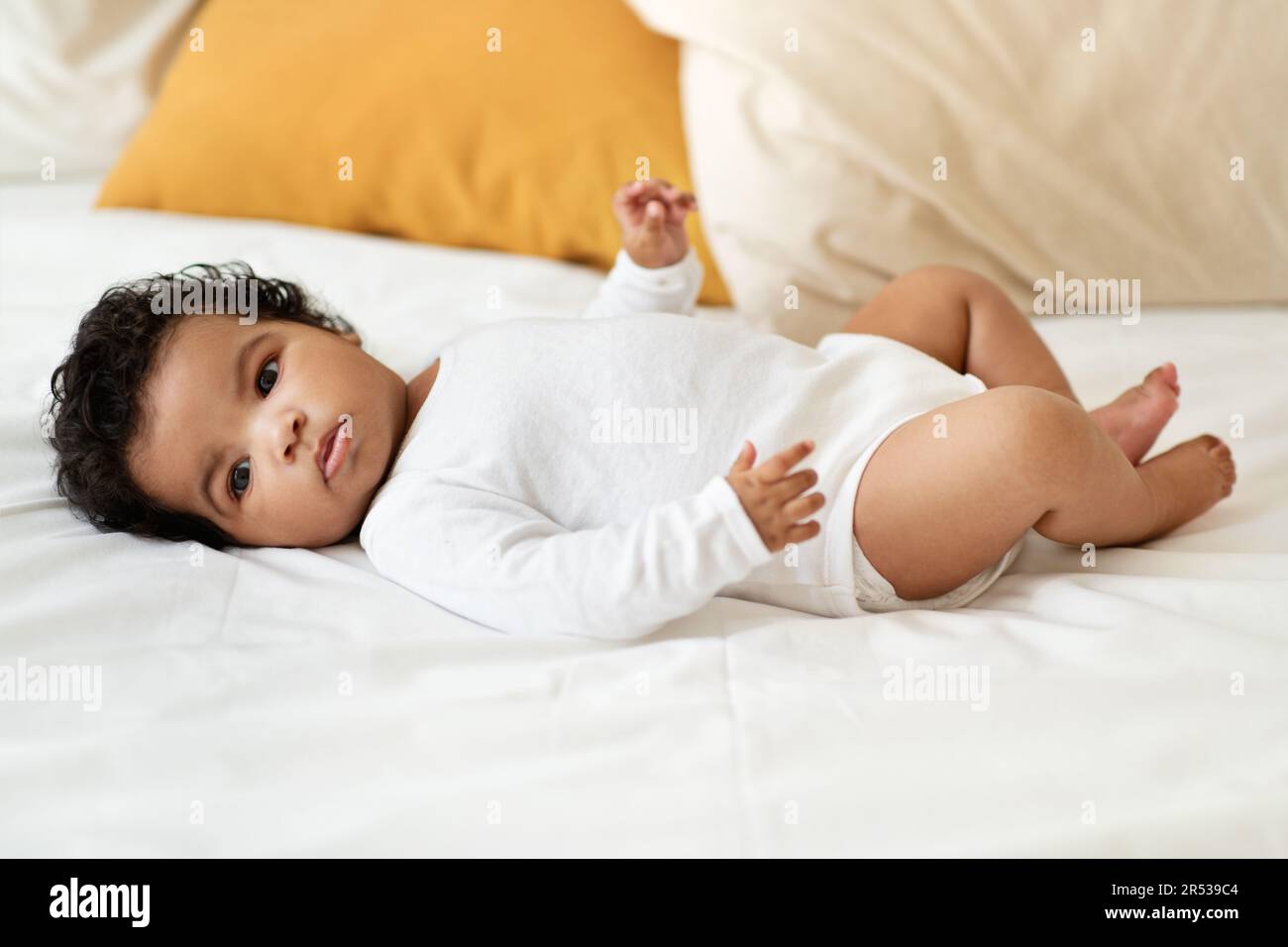 Petit enfant noir sérieux fille ou garçon dans les vêtements se trouve sur blanc confort lit dans la chambre. Soins de santé, nouveau-né Banque D'Images