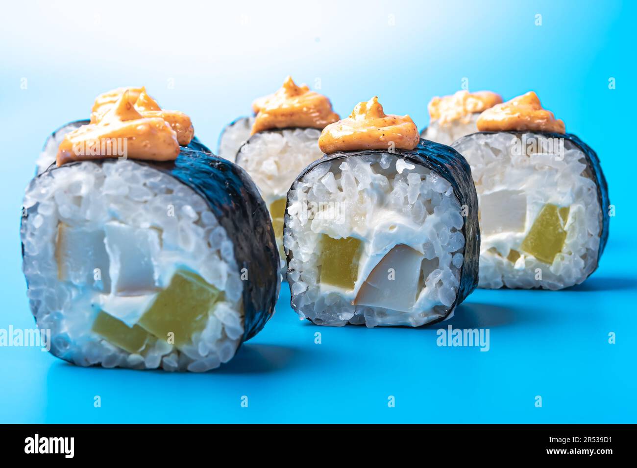 Petits pains à sushi au thon, au daikon, au fromage et à la sauce épicée, sur fond bleu. Photo de haute qualité Banque D'Images