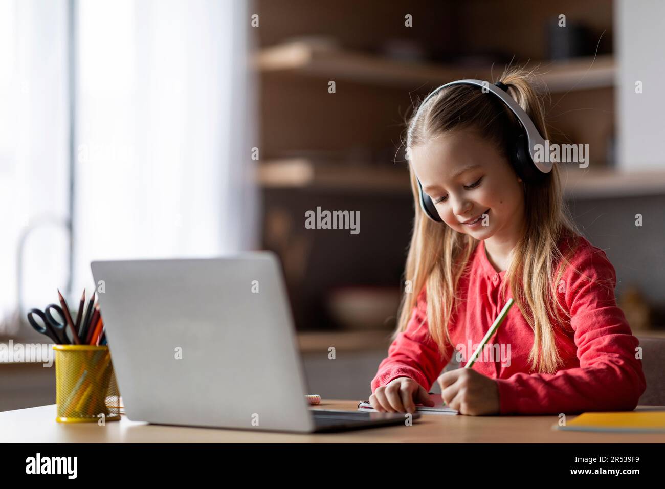 L'éducation à distance. Petite fille dans l'étude de casque avec ordinateur portable et de prendre des notes Banque D'Images