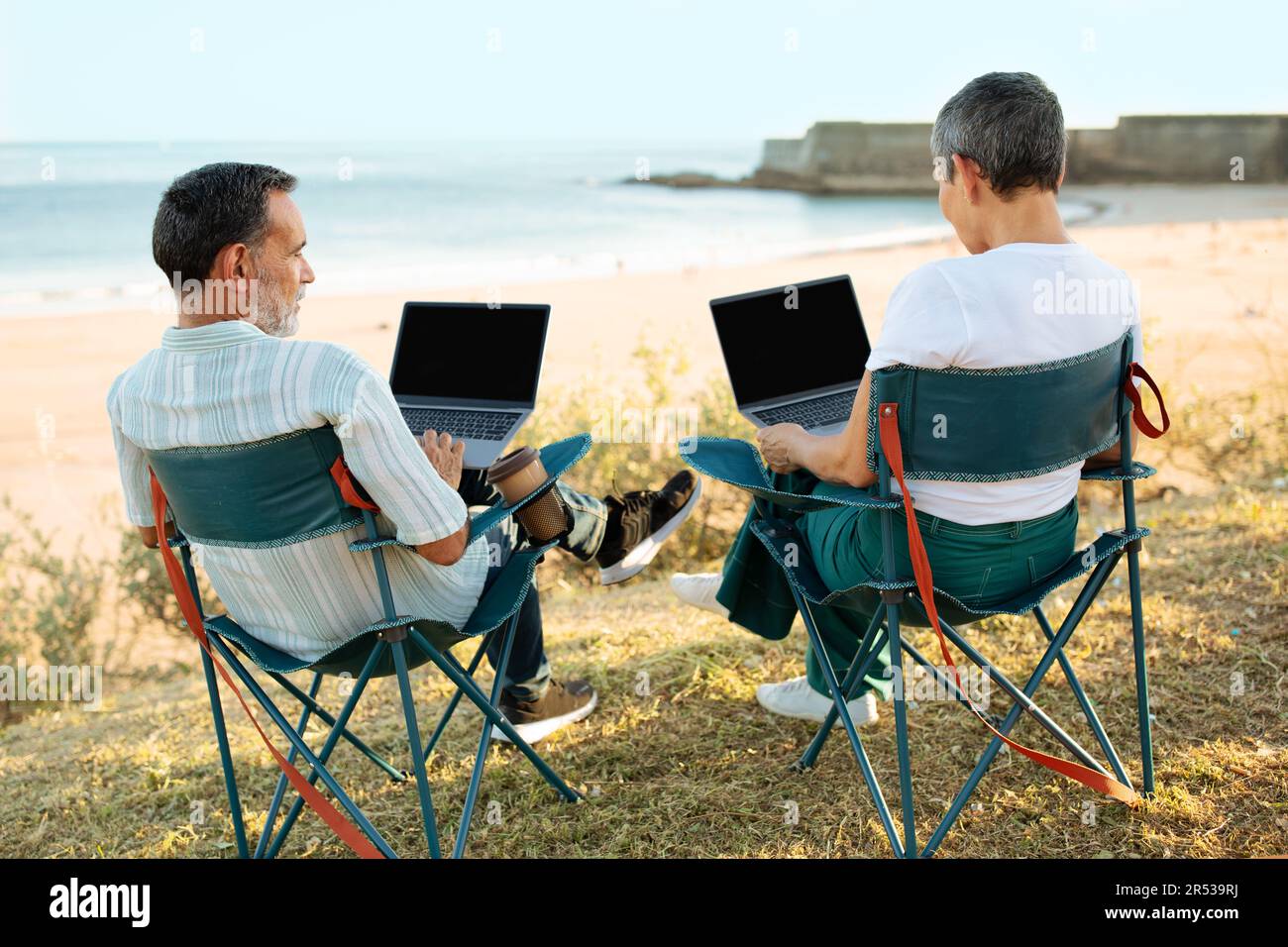Des indépendants expérimentés se coupent en utilisant des ordinateurs portables travaillant en ligne en extérieur près de l'océan Banque D'Images