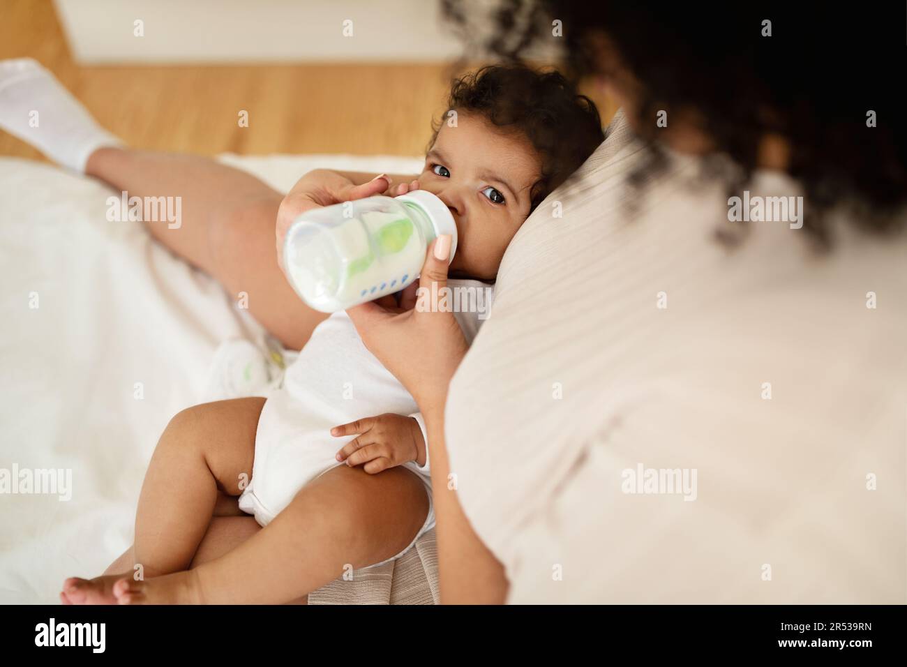 La mère millénaire noire se nourrit de bébé affamé de biberon sur un lit blanc, aime l'amour et le confort Banque D'Images