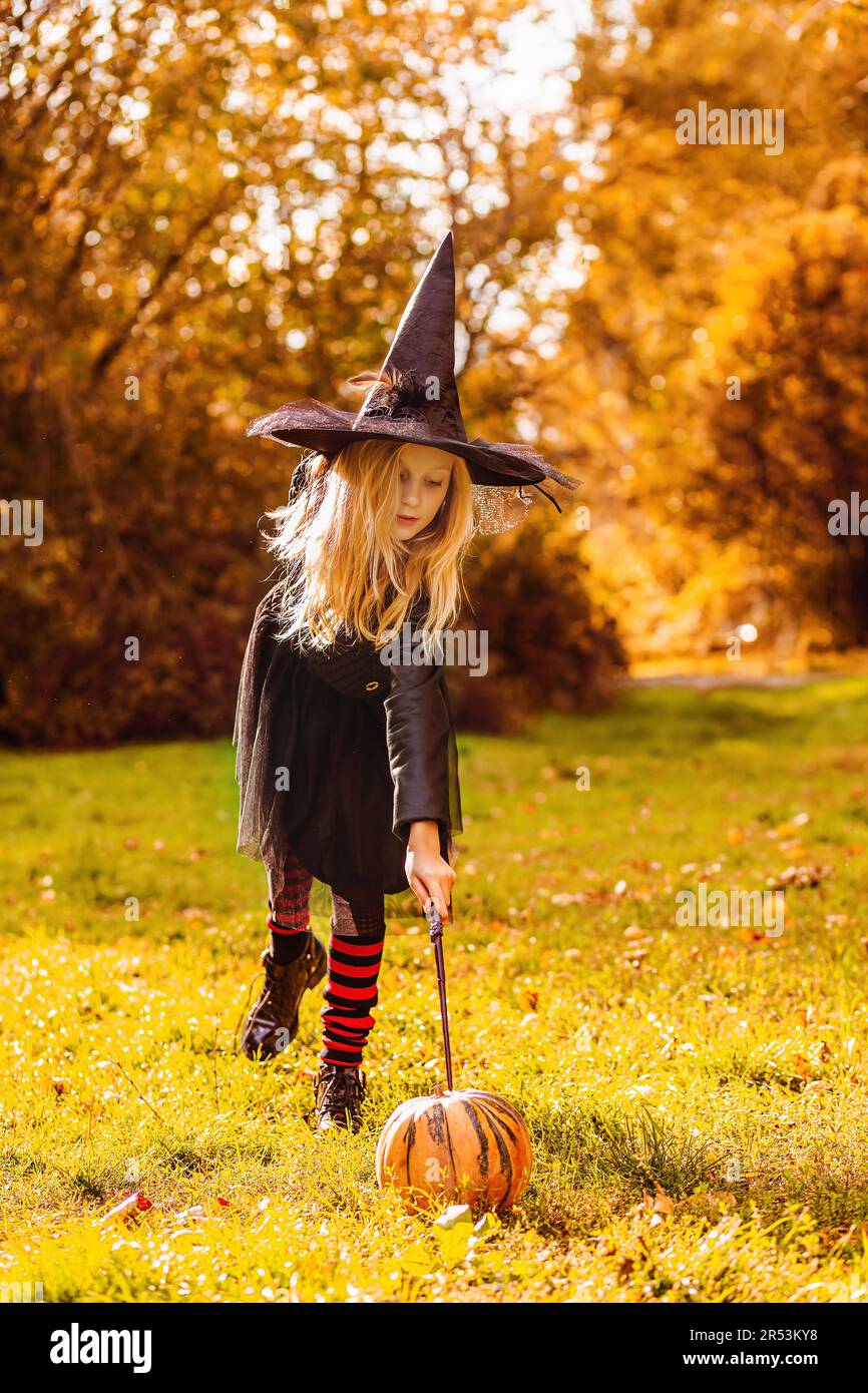 Une fille dans un costume de sorcière dit un sort et enchante une citrouille avec une baguette magique. Banque D'Images