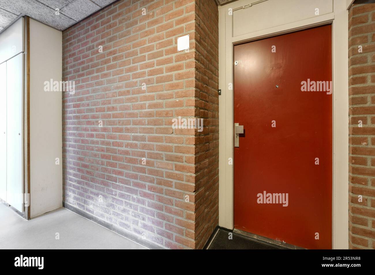 une porte rouge dans un mur de briques qui a été peint pour ressembler à ce qu'il se passe sur le côté d'un bâtiment Banque D'Images